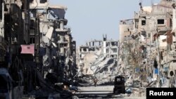 FILE - A fighter of the Syrian Democratic Forces stands amid the ruins of buildings near the Clock Square in Raqqa, Syria, Oct. 18, 2017.