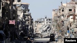 FILE - A fighter of the Syrian Democratic Forces stands amid the ruins of buildings near the Clock Square in Raqqa, Syria, Oct. 18, 2017.