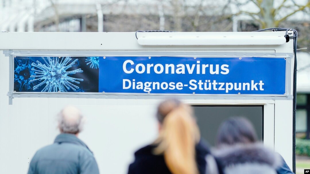 People stand in front of containers with a banner reeding "Coronavirus Diagnosis Base" on the grounds of the University Hospital in Mannheim, Germany, March 11, 2020.