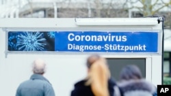 People stand in front of containers with a banner reeding "Coronavirus Diagnosis Base" on the grounds of the University Hospital in Mannheim, Germany, March 11, 2020.