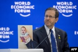 Presiden Israel Isaac Herzog menunjukkan foto bayi berusia 10 bulan Kfir Bibas yang dipegang oleh Hamas selama sesi pertemuan Forum Ekonomi Dunia (WEF) di Davos pada 18 Januari 2024. (Foto: AFP)