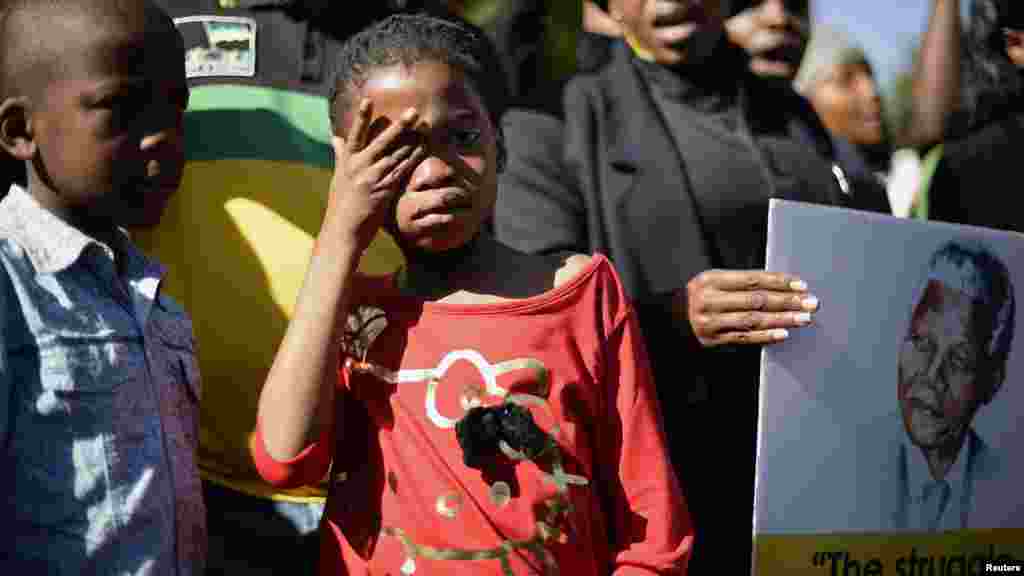 A girl weeps as she stands next to a portrait of Nelson Mandela.