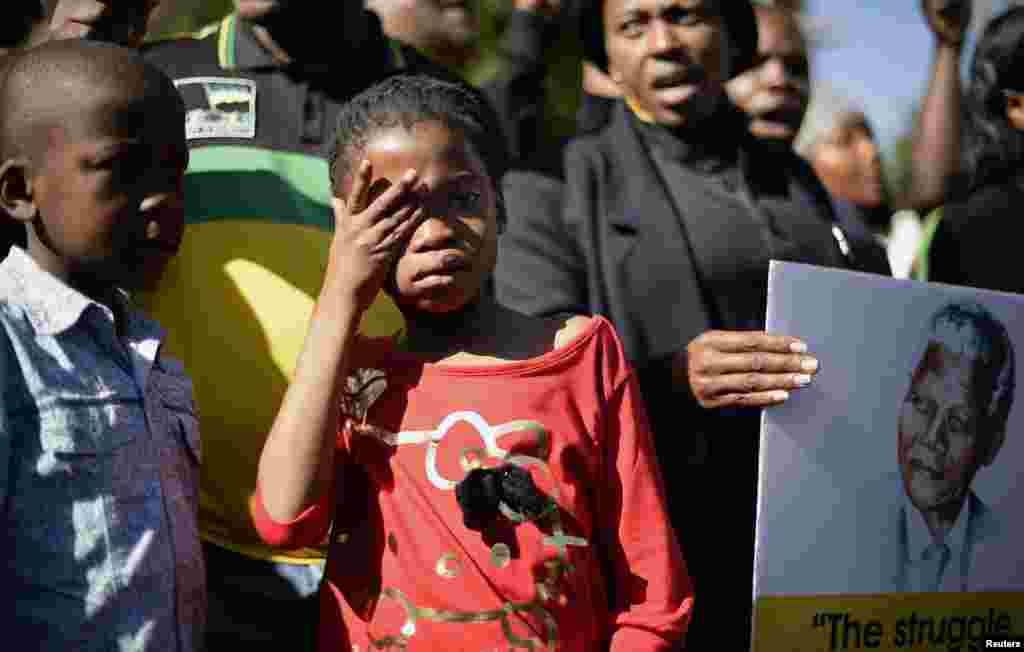 A girl weeps as she stands next to a portrait of Nelson Mandela.