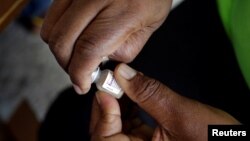 FILE - A member of a vaccination campaign against cholera opens a vial.