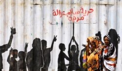 FILE - People walk past graffiti reading in Arabic "Freedom, Peace, Justice and Civilian" rule in the Burri district of Khartoum, Sudan, July 10, 2019.