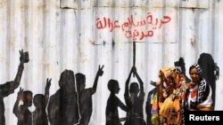 People walk past graffiti reading in Arabic "Freedom, Peace, Justice and Civilian" in the Burri district of Khartoum, Khartoum, Sudan.