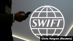 CANADA -- A man using a mobile phone passes the logo of global secure financial messaging services cooperative SWIFT at the SIBOS banking and financial conference in Toronto, Ontario, October 19, 2017