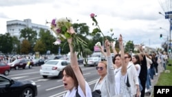 Women with flowers stand along a street as they protest police violence during recent rallies of opposition supporters, who accuse strongman Alexander Lukashenko of falsifying the polls in the presidential election, in Minsk, Aug. 13, 2020. 