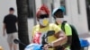 People wearing protective face masks ride a scooter down Ocean Drive amid the coronavirus pandemic, July 12, 2020, in Miami Beach, Fla.