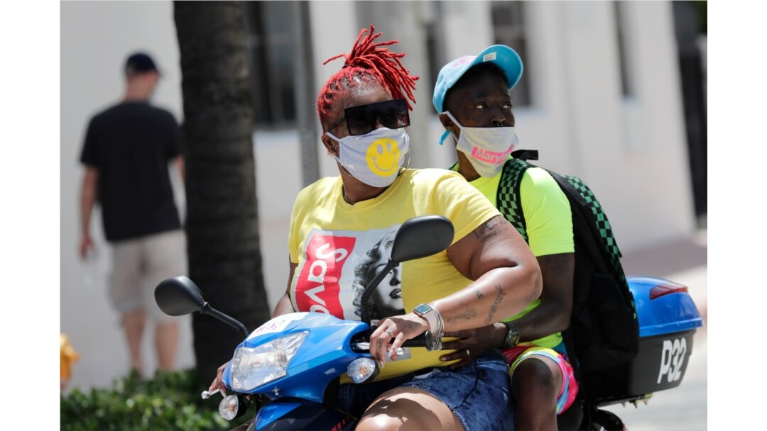 People wearing protective face masks ride a scooter down Ocean Drive during the coronavirus pandemic, Sunday, July 12, 2020, in Miami Beach, Fla.