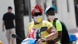 People wearing protective face masks ride a scooter down Ocean Drive during the coronavirus pandemic, Sunday, July 12, 2020, in Miami Beach, Fla.