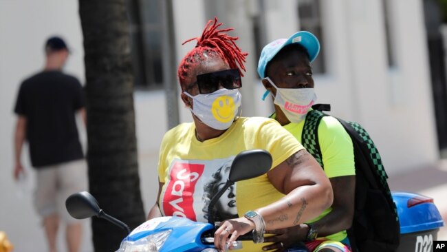 People wearing protective face masks ride a scooter down Ocean Drive during the coronavirus pandemic, Sunday, July 12, 2020, in Miami Beach, Fla. Florida on Sunday reported the largest single-day increase in positive coronavirus cases in any one…