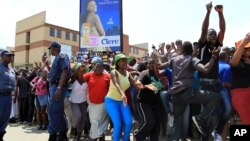 FILE - Police officers watch as crowds of people gather outside a police station in the Diepsloot area, north of Johannesburg, South Africa.