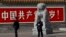 Kineski policajci u civilu i uniformi ispred panoa na kome piše "Živela Kineska komunistička partija"