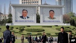 people walk beneath portraits of late leaders, Kim Il Sung, left, and Kim Jong Il, in Pyongyang, North Korea, April 18, 2017.