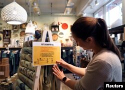 An employee places a sign with instructions about social distancing as she prepares to reopen a shop in the district of Prenzlauer Berg after a partial end of the lockdown in Berlin, April 18, 2020.