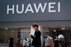 FILE -People walk past a Huawei retail store in Beijing, June 30, 2019.