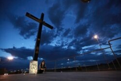 A woman sits next to a sign with a message that reads: ¨No More Guns! Make Love¨, in Juarez, Mexico, Aug. 3, 2019, where people are gathering for a vigil for the 3 Mexican nationals who were killed in an El Paso shopping-complex shooting.