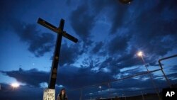 A woman sits next to a sign with a message that reads: ¨No More Guns! Make Love¨, in Juarez, Mexico, Aug. 3, 2019, where people are gathering for a vigil for the 3 Mexican nationals who were killed in an El Paso shopping-complex shooting.