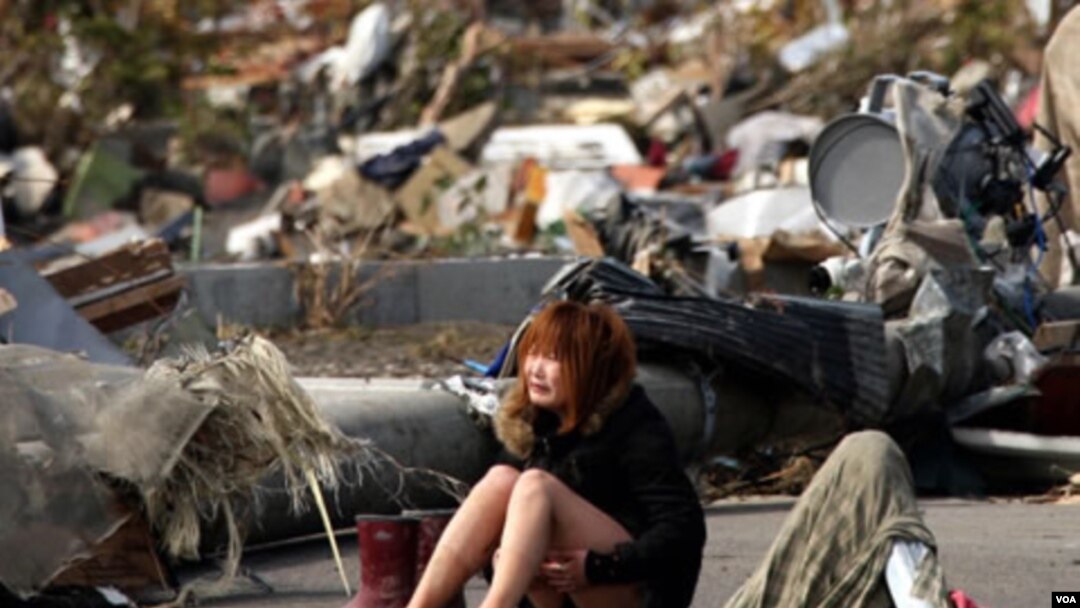 Seorang perempuan duduk menangis di tengah-tengah kerusakan akibat gempa dan tsunami, Senin (14/3).