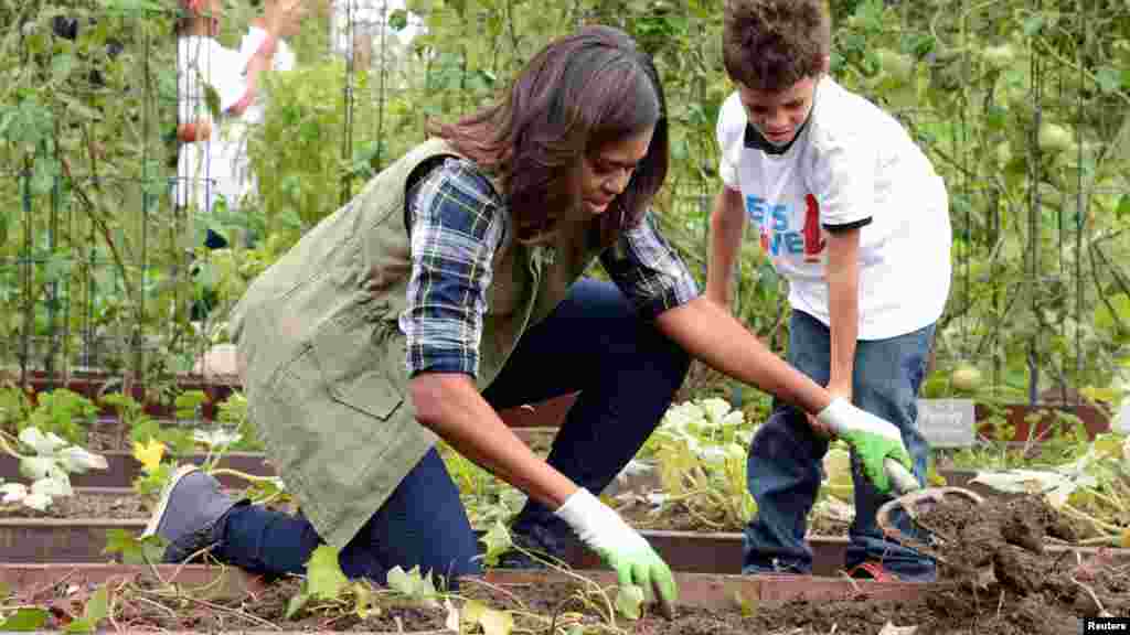 Ibu Negara Michelle Obama membantu seorang siswa memanen sayuran di kebun dapur Gedung Putih (6/10). (Reuters/Mike Theiler)