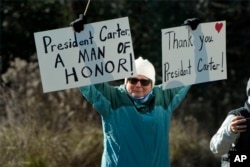 A person holds signs as the hearse containing the casket of former President Jimmy Carter, pauses at the Jimmy Carter Boyhood Farm in Archery, Georgia, Jan. 4, 2025.