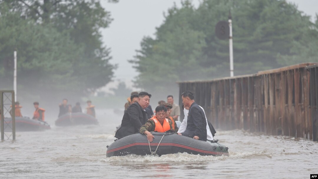 Pemimpin Korea Utara Kim Jong Un (kiri) mengendarai perahu karet melewati banjir saat ia memeriksa kerusakan di wilayah tersebut setelah hujan lebat yang memecahkan rekor pada 29 Juli di Kota Sinuiju di Provinsi Pyongan Utara. (Foto: KCNA VIA KNS/AFP)