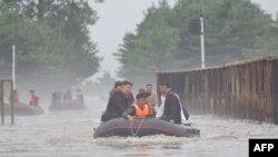 Pemimpin Korea Utara Kim Jong Un (kiri) mengendarai perahu karet melewati banjir saat ia memeriksa kerusakan di wilayah tersebut setelah hujan lebat yang memecahkan rekor pada 29 Juli di Kota Sinuiju di Provinsi Pyongan Utara. (Foto: KCNA VIA KNS/AFP)