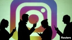 In this file photo, silhouettes of mobile users are seen next to a screen projection of the Instagram logo in this picture illustration taken March 28, 2018. (REUTERS/Dado Ruvic/Illustration/File Photo)