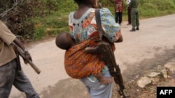 Une jeune femme combattant avec le bataillon Mai Mai à Irangi, dans le district de Bunyakiri au Sud-Kivu en RDCongo, porte son fusil et son fils le 14 janvier 2004.