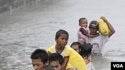 Warga menggendong anak-anak mereka saat melintasi daerah mereka yang terendam banjir akibat topan Nesat (Pedring) di desa Tanza, Malabon, utara Manila (27/9).