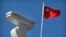 FILE - A Chinese flag flies near a Hikvision security camera monitoring a traffic intersection in Beijing, Oct. 8, 2019. 