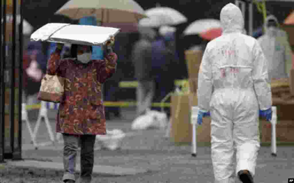 A woman carries a heat blanket as she leaves a radiation emergency scanning center in Koriyama, Japan, Tuesday, four days after a giant quake and tsunami struck the country's northeastern coast, March 15, 2011 – (AP)