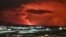 Houses in the village of Hafnarfjordur is seen as smoke is billowing in the distance as the lava colour the night sky orange from an volcanic eruption on the Reykjanes peninsula, western Iceland on December 18, 2023.