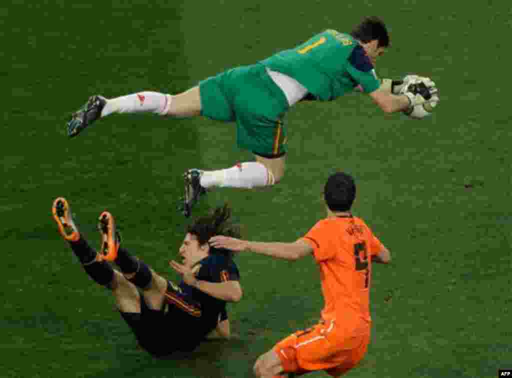 Spain goalkeeper Iker Casillas, top, makes a save over Netherlands' Robin van Persie, right, and Spain's Carles Puyol during the World Cup final soccer match between the Netherlands and Spain at Soccer City in Johannesburg, South Africa, Sunday, July 11,