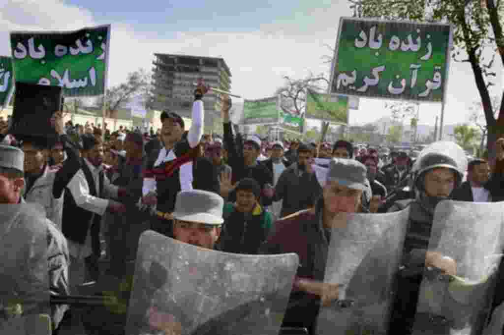 Afghans shout anti- US slogans, behind a row of policemen, during a demonstration in Kabul, Afghanistan on Friday, April. 1, 2011. Eight foreigners were killed on Friday after demonstrators protesting a reported burning of the Muslim holy book stormed a