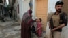 A police officer stands guard as a health worker, center, administers a polio vaccine to a child in a neighborhood of Peshawar, Pakistan, Oct. 28, 2024.