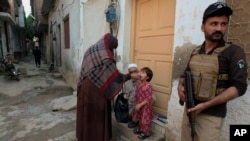 A police officer stands guard as a health worker, center, administers a polio vaccine to a child in a neighborhood of Peshawar, Pakistan, Oct. 28, 2024.