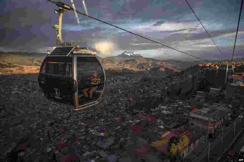 People ride a cable car, with La Paz and the Illimani mountain seen in the background, in El Alto, Bolivia, Oct. 17, 2019.