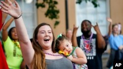 Hayley Bosarge vies for items tossed by parade participants as she holds her daughter Ellie Bosarge, 2, during "Tardy Gras," a compensation for a COVID-canceled Mardi Gras, in Mobile, Ala., May 21, 2021. 