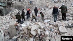Orang-orang berdiri di atas puing-puing bangunan yang hancur pascagempa, sementara pencarian korban berlanjut, di Aleppo, Suriah (foto: dok). 