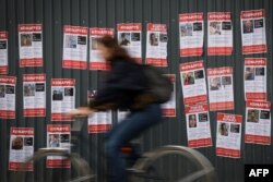 Osoba na biciklu u Parizu prolazi pored postera sa slikama i imenima nestalih u Izraelu.