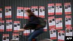 Osoba na biciklu u Parizu prolazi pored postera sa slikama i imenima nestalih u Izraelu