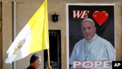 Un sacerdote cristiano con una bandera del Vaticano pasa junto a un póster del papa Francisco en la iglesia Mar Youssif, en Bagdad, durante los preparativos para la visita del Pontífice a Irak. Febrero 26 de 2021.