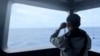 FILE - In this undated photo released by the Indonesian Maritime Security Agency, an agent uses binoculars to monitor the movement of a Chinese coast guard vessel in the waters of North Natuna Sea in the disputed area of the South China Sea, Indonesia, on Oct. 24, 2024. 