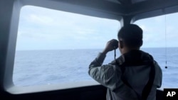 FILE - In this undated photo released by the Indonesian Maritime Security Agency, an agent uses binoculars to monitor the movement of a Chinese coast guard vessel in the waters of North Natuna Sea in the disputed area of the South China Sea, Indonesia, on Oct. 24, 2024. 