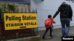 Seorang pria dan anak laki-laki berjalan melewati papan petunjuk TPS menjelang Pemilu referendum untuk menetapkan hukum soal Aborsi tanggal 25 Mei mendatang di Dublin, Irlandia, 22 Mei 2018. 