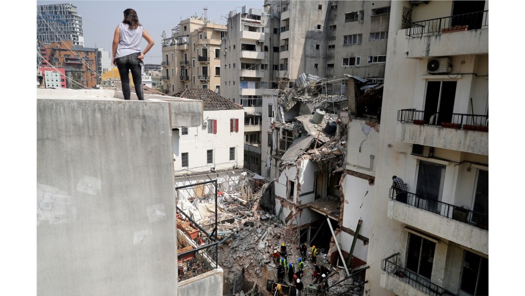 FILE - A woman looks on from a rooftop as rescue workers dig through the rubble of a badly damaged building in Lebanon's capital Beirut, Sept. 4, 2020.