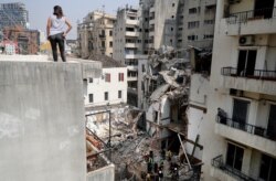 FILE - A woman looks on from a rooftop as rescue workers dig through the rubble of a badly damaged building in Lebanon's capital Beirut, Sept. 4, 2020.