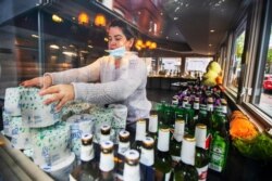 Sarah Rivas, an employee at Annie's Paramount Steakhouse in Dupont Circle district of Washington, arranges a display of toilet paper and liquor for carry out orders, April 13, 2020.